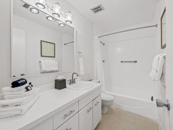 This image shows a clean, white bathroom with a bathtub, sink, mirror, and countertop. Towels are neatly folded on the counter and a towel bar.