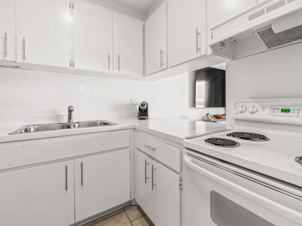 A modern white kitchen with cabinets, an electric stove, a sink, and a coffee maker on the counter, featuring a clean and minimalist design.