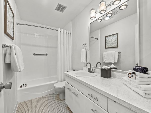This image shows a clean, white bathroom with a vanity, mirror, bathtub, shower curtain, towels, and a well-lit environment.