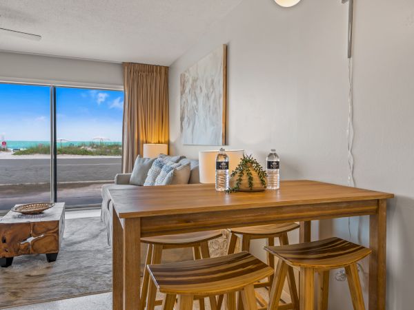 A cozy living area with a wooden dining table, stools, sofa, coffee table, and large window showing a scenic outdoor view ends the sentence.