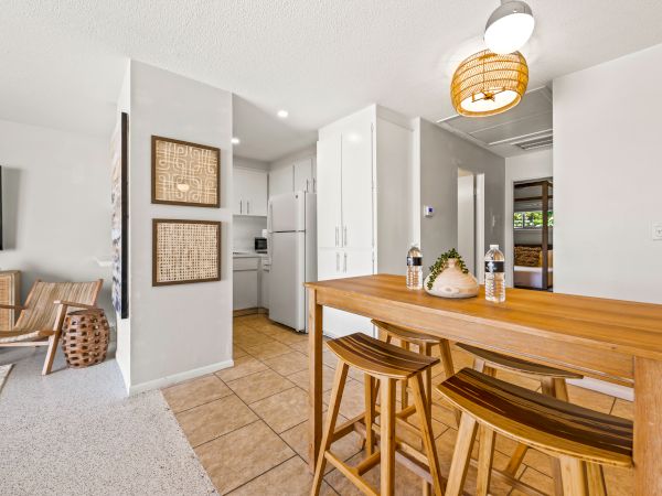 The image shows a modern kitchen and dining area with wooden furniture, decorated wall art, and white cabinets. Cozy and minimalistic design.