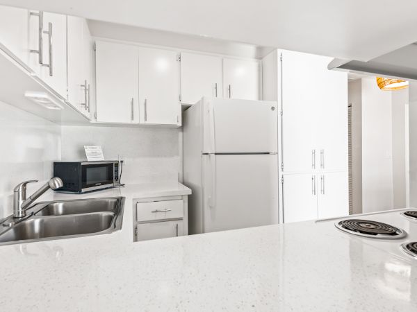 A modern white kitchen features a sink, stove, refrigerator, microwave, and ample cabinetry for storage.