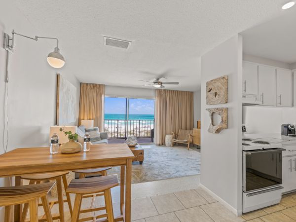 A modern beachfront studio apartment with a kitchen, dining area, and living space leading to a balcony showing the ocean view.