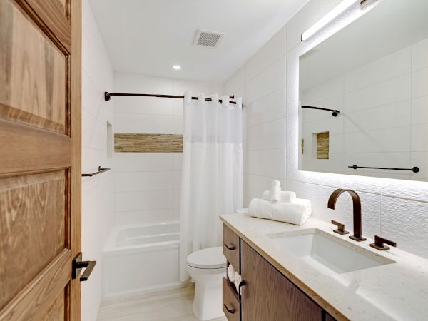 A modern bathroom featuring a wooden door, a vanity with a sink and mirror, a shower-tub combo with a white curtain, and neatly rolled towels.