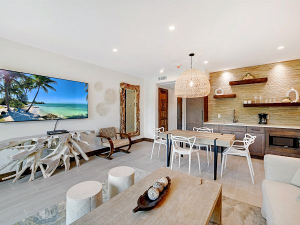 A modern living room features a wall-mounted TV, a unique driftwood console table, a dining area, a small kitchenette, and stylish decor.