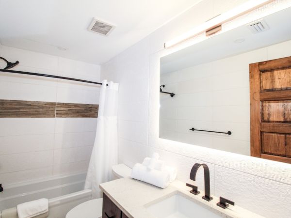 A modern bathroom with a bathtub, shower curtain, sink, large mirror, towels, and wooden door.