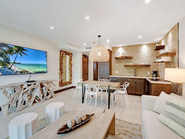 A modern living room with a large TV, unique wood furniture, a kitchen area, a dining table with chairs, and a cozy couch.