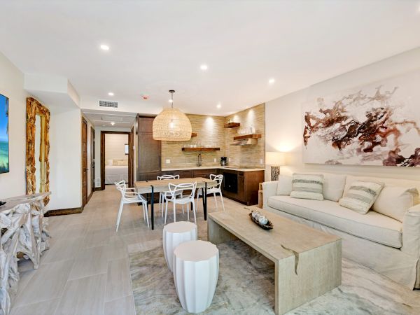 A modern living room and kitchen with neutral tones, art on the wall, TV, dining table, and a cozy seating area with a sofa and coffee table.