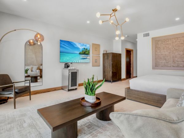 A modern, airy hotel-like living room with a white palette, wooden accents, a TV wall, a low wooden coffee table, plants, and a cozy seating area.