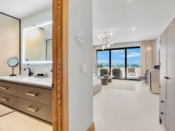 A modern hotel suite with a double vanity, stylish decor, and a bright living area with a balcony overlooking the ocean.
