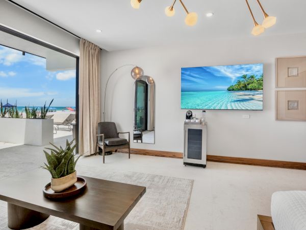 Luxurious bright living room with a beach view, modern furniture, a wall TV, potted plants, and a sliding door opening to a sunny balcony.