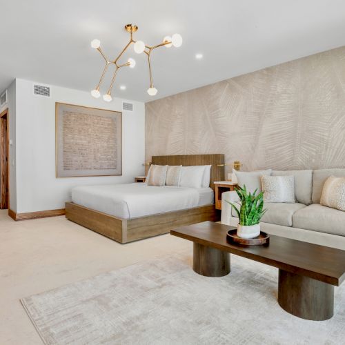 A cozy living room with a stone fireplace, wooden beams, a small coffee table, and a mix of rustic and modern furnishings, plus a large rug.