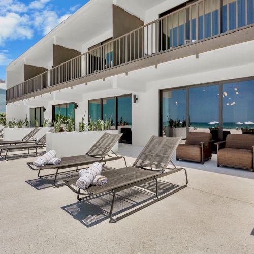 A sunny poolside scene at a resort with lounge chairs, a blue pool, and a modern building with balconies.