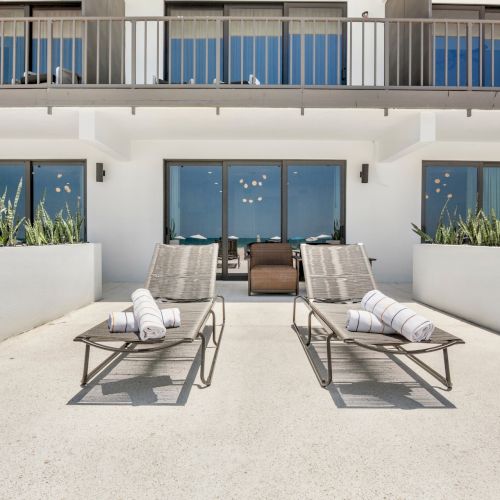 A bright outdoor patio with sun loungers, potted succulents, and blue curtains behind sliding doors.