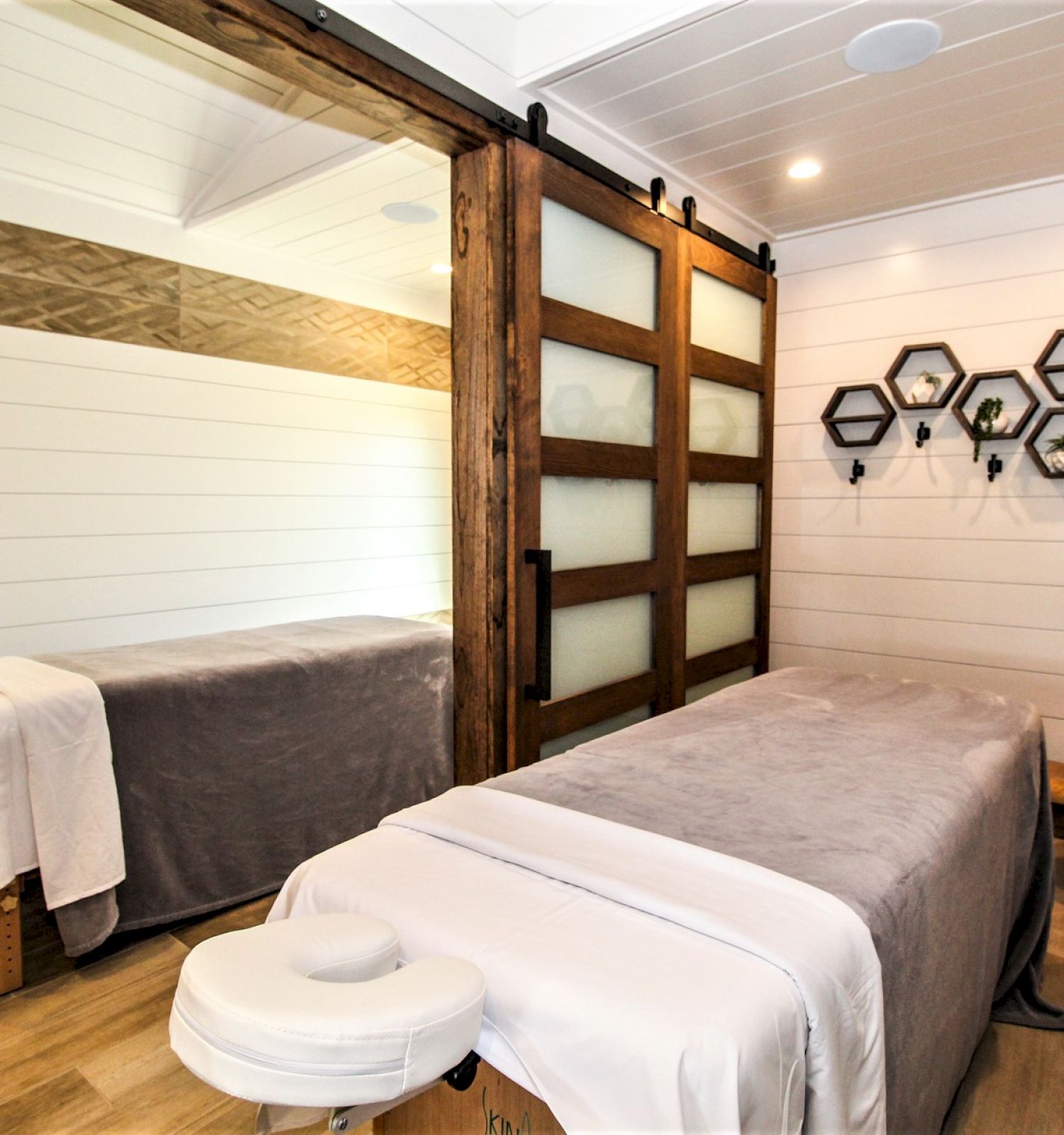 A cozy massage room with a neatly prepared massage table, hexagonal wall decor, wooden accents, and soft lighting creates a relaxing ambiance.