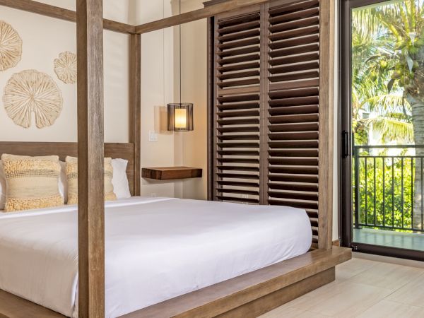 A modern bedroom with a canopy bed, decorative pillows, wall art, and a view of a balcony with palm trees outside.